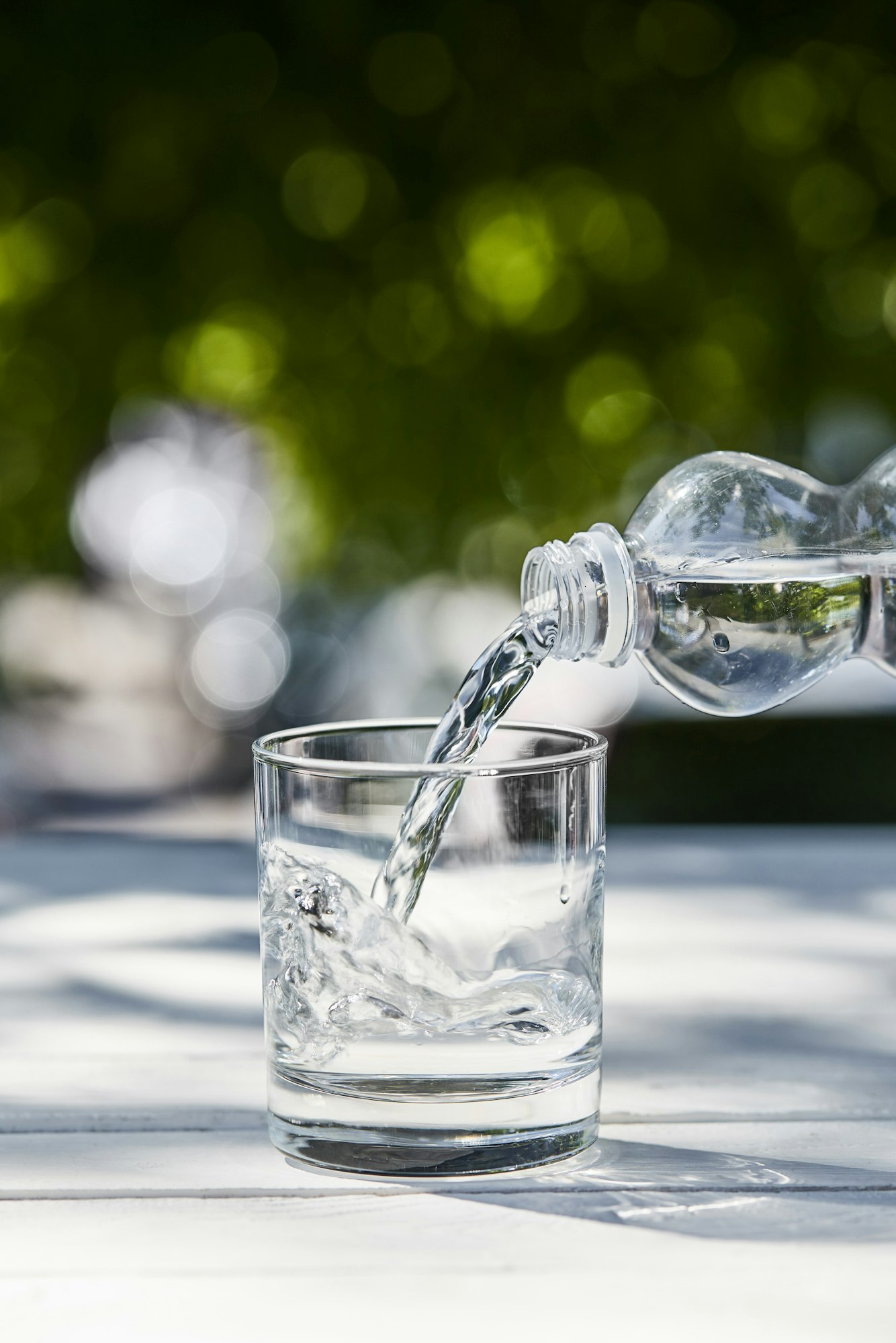 fresh clean water pouring from bottle in transparent glass at sunny day on wooden table